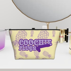 Op de afbeelding: Een gele ritszak met een paars ananaspatroon en de tekst "COOCHIE PLUGS" in paars.