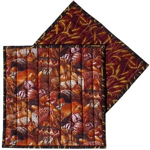 May include: Two quilted pot holders. One is brown with a pattern of various breads and rolls. The other is burgundy with a gold wheat pattern.