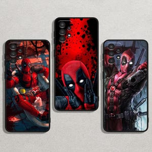 May include: Three black phone cases featuring Deadpool artwork. The cases display Deadpool in various action poses, with a red and black color scheme. One case shows Deadpool giving a hand gesture, another shows him holding a gun, and the third shows him in a seated position.