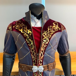 May include: A purple and red jacket with gold embroidery and a brown belt. The jacket has a high collar and long sleeves.