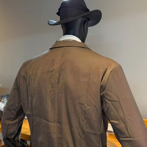 May include: A brown blazer and a black fedora hat on a mannequin. The mannequin is wearing a white collared shirt. The blazer has a classic design and the hat has a wide brim. The mannequin is set against a neutral background.