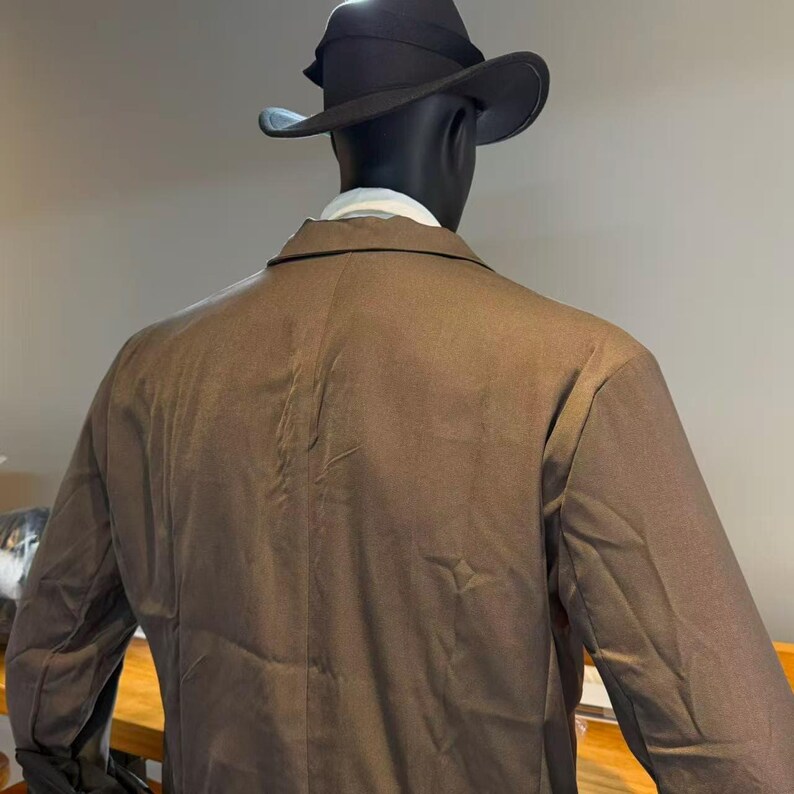 May include: A brown blazer and a black fedora hat on a mannequin. The mannequin is wearing a white collared shirt. The blazer has a classic design and the hat has a wide brim. The mannequin is set against a neutral background.