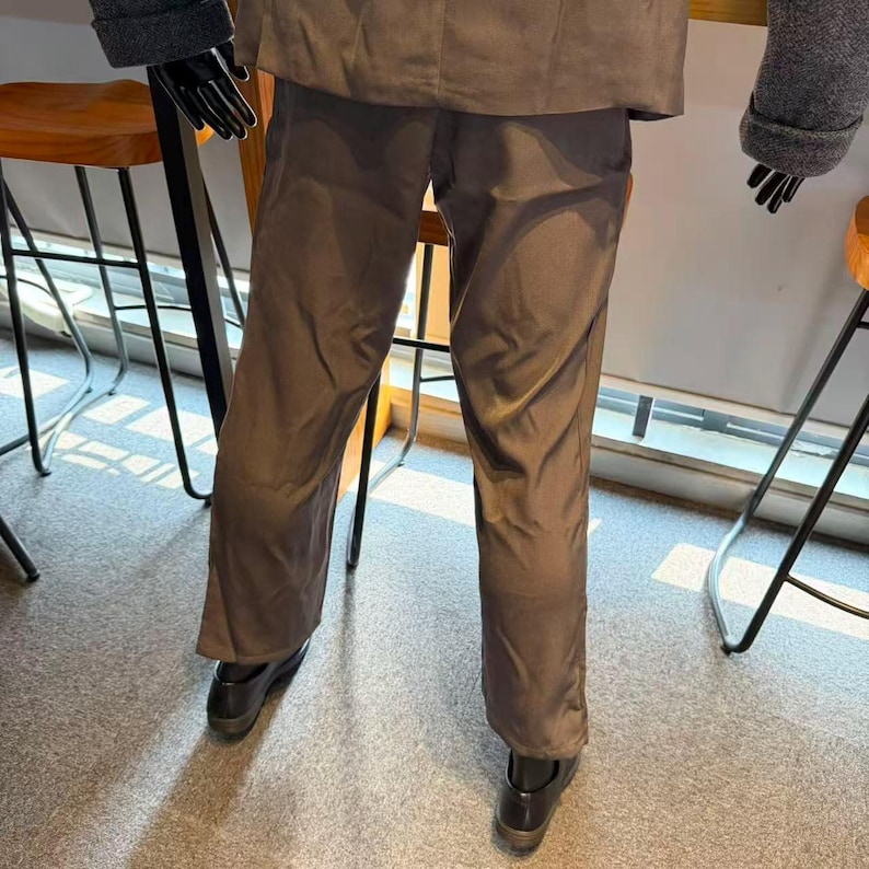 May include: A brown suit with matching pants and jacket. The pants are straight-legged and the jacket has a classic cut. The suit is paired with black shoes. The mannequin is wearing black gloves.