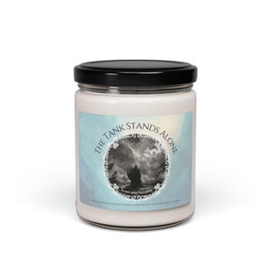 May include: A white candle jar with a black lid. The label on the jar features a blue background with a circular design and the text "The Tank Stands Alone".