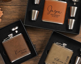 May include: Three personalized leather flasks with shot glasses and funnels in black boxes. The flasks are engraved with names and dates. One flask is tan, one is brown, and one is a lighter brown color. The shot glasses are silver.