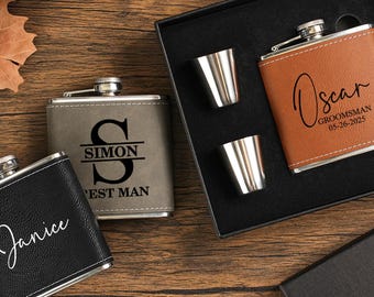 May include: A collection of personalized flasks in black, gray, and brown leather. One flask is engraved with "Janice", another with "Simon" and "Best Man", and a third with "Oscar" and "Groomsman". The set includes shot glasses and a funnel.