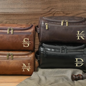May include: Four leather wash bags in shades of brown and black, each with a zippered main compartment and a front pocket. The bags are personalized with gold lettering: "Simon", "Nestor", "Kenya", and "Devin".