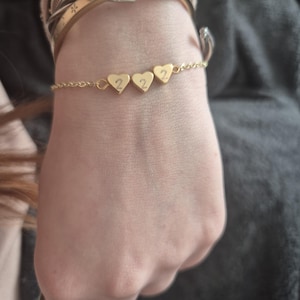 Pu&ograve; includere: Un braccialetto dorato con tre ciondoli a forma di cuore, ognuno con il numero "2". Il braccialetto a catena sottile &egrave; visibile su un polso, insieme ad altri braccialetti dorati. Il design &egrave; semplice ed elegante.
