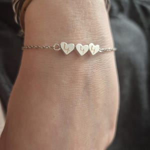 Pu&ograve; includere: Un braccialetto d'argento con tre ciondoli a forma di cuore. Ogni ciondolo ha inciso il numero "4". Il braccialetto &egrave; indossato su un polso, con altri braccialetti visibili sullo sfondo.