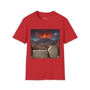 Può includere: T-shirt rossa con una grafica di Pompei e un'eruzione vulcanica. Il design include la parola "Pompei" e frasi latine su tavole di pietra. La maglietta ha anche il testo "LM73" in alto.