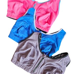May include: Three sports bras in pink, blue, and gray with a front zipper closure. The bras are layered on top of each other.