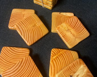May include: Set of eight wooden coasters with a natural wood grain pattern. The coasters are square and have a light brown color. The coasters are stacked in a pile, with a piece of twine tied around them.