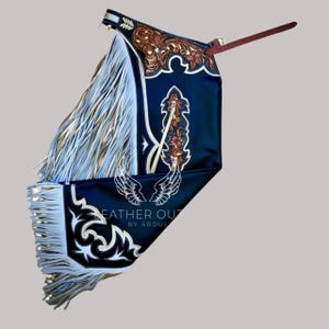 May include: A black leather chaps with white and gold fringe. The chaps feature intricate floral and scrollwork designs in brown and white. The text "LEATHER OUT BY ABDUL" is visible on the bottom of the chaps.