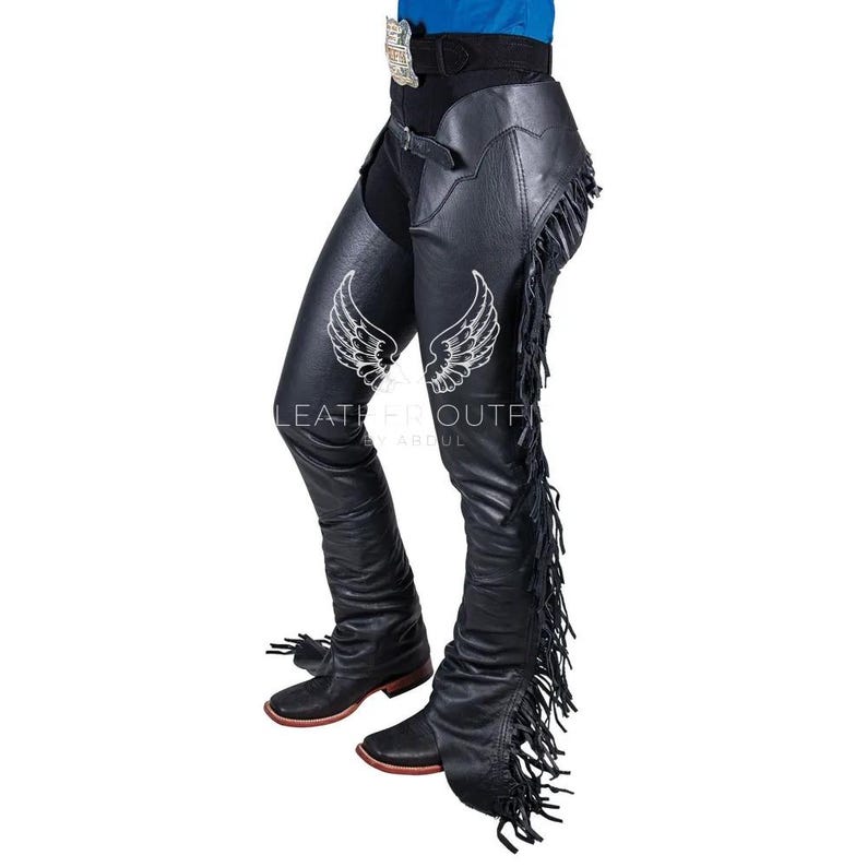 May include: Black leather chaps with white embroidered wing designs. The chaps feature fringe along the outer seams and are worn with a belt and boots. The image includes the text "LEATHER FIT OUTFIT BY ABDUL".