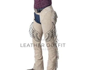 Op de afbeelding: Beige suède chaps met franjes. De chaps worden gedragen over een spijkerbroekshort en hebben een riem met een zilveren gesp. De afbeelding bevat de tekst "LEATHER OUTFIT BY ABDUL".