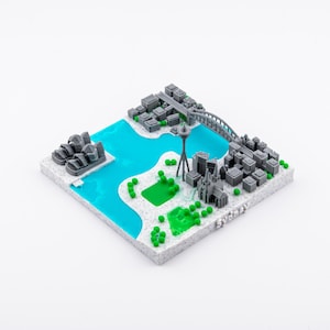 Può includere: Un modello 3D stampato di una città, con monumenti iconici, un ponte ed edifici. Il modello include un corpo d'acqua turchese, alberi verdi e una base grigia. La parola "Sydney" è stampata sulla base.