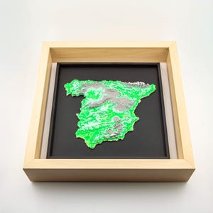 May include: A framed 3D map of Spain, showcasing the country's topography in vibrant green and gray. The map is set against a black background within a light-colored wooden frame, creating a striking visual contrast.