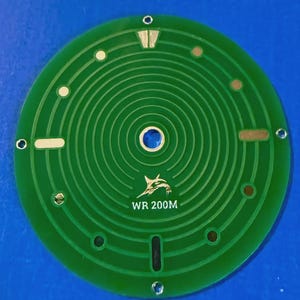 May include: Two watch dials, one green and one white, are displayed against a blue background. The green dial has concentric circles and the text "WR 200M". The white dial also has the text "WR 200M".