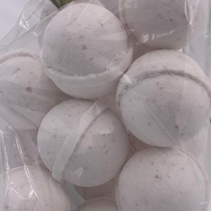 May include: A clear plastic bag filled with several white, spherical bath bombs. Each bath bomb has a textured surface and a light-colored band around the middle. The bath bombs appear to be a natural, spa-like product.