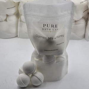 May include: A white bag of bath bombs with the text "PURE BATH LAB Oatmeal, Milk & Honey". The bag contains 14 bath bombs, weighing 17 oz. Several bath bombs are visible outside the bag.