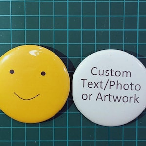 May include: Two circular badges. One is yellow with a smiling face. The other is white with the text "Custom Text/Photo or Artwork" in black. They are displayed on a green grid.
