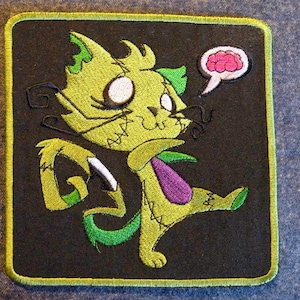 May include: Green and purple stitched cartoon cat with a thought bubble above its head. The thought bubble is pink and contains a brain shape. The cat is holding a knife in its right paw.