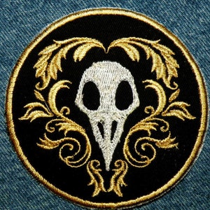 May include: A black and gold embroidered patch with a white skull and floral design.