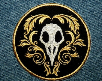 May include: A black and gold embroidered patch with a white skull and floral design.