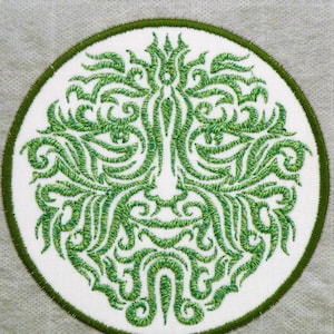 May include: A green embroidered patch with a stylized face design. The face is made up of swirling lines and patterns, creating a unique and intricate design.