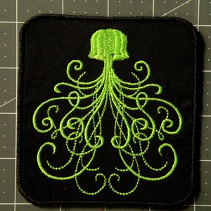 May include: Green embroidered patch of an octopus with curly tentacles on a black background.