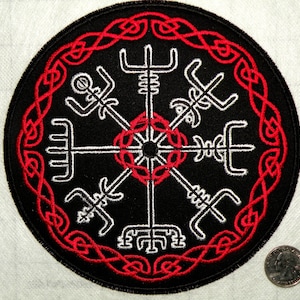 May include: A black and white embroidered patch with a red Celtic knot border. The center of the patch features a white compass with eight points, each point with a stylized design.