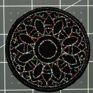 May include: Black round patch with a silver glitter design of a circular mandala with a smaller circle in the center.