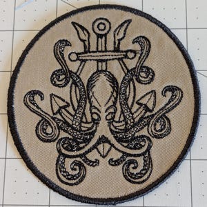 May include: A beige embroidered patch with a black octopus wrapped around an anchor and trident. The octopus has a detailed design with swirling tentacles.