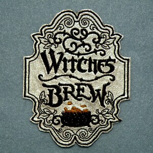 May include: A silver and black embroidered patch with the text "The Witches Brew" and a black cauldron with orange flames.