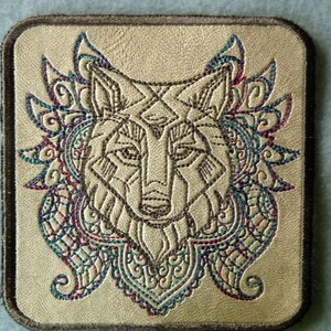 May include: A beige leather patch with a brown border features an embroidered wolf head with intricate, colorful floral designs around it.