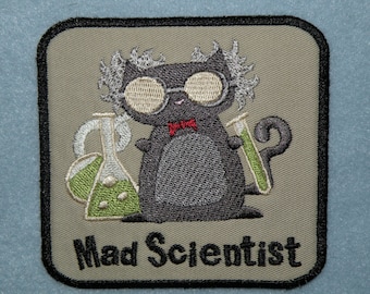 Op de afbeelding: Een geborduurde patch in grijs en zwart met een cartoonkat die een bril en een rode strik draagt. De kat houdt een groene reageerbuis en een groene beker vast. De tekst "Mad Scientist" staat onder de kat.