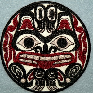 May include: A round embroidered patch with a stylized black and red design of a creature with large eyes and a wide mouth. The background is white.