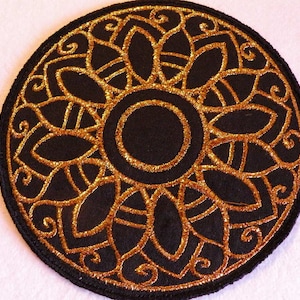 May include: A black fabric patch with a gold embroidered mandala design. The mandala features a central circle surrounded by intricate floral patterns.