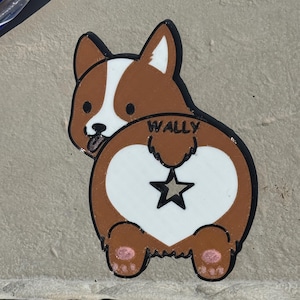 May include: A brown and white corgi-shaped sticker with the name "WALLY" above a white heart with a black star. The corgi is depicted from the rear, with pink paw pads and a black outline.