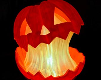 May include: A bright orange jack-o'-lantern sculpture with a carved face and a jagged, open top section. The interior glows with a warm, white light that illuminates the textured, flowing structure emerging from the center of the pumpkin.