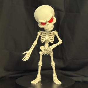 May include: A cream-colored articulated skeleton figurine featuring a large, stylized cranium and prominent, glowing red eyes. The figure stands in an upright position with one arm extended outward and the other bent at the elbow.
