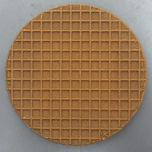 May include: A round, brown coaster with a waffle pattern. The coaster is made of a solid material and has a grid-like texture across its entire surface. The edges are slightly rounded.
