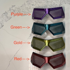 May include: Four pairs of decorative eyewear in purple, green, gold, and red. Each pair features a mesh design and a geometric shape. The colors are labeled with arrows pointing to each pair.