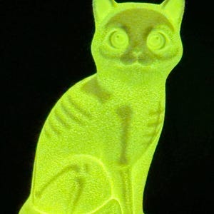 May include: A glowing neon yellow cat figurine with a textured surface. The cat is depicted in a seated position, featuring visible skeletal rib and leg bone patterns illuminated in a brighter shade of yellow against a solid black background.