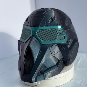 May include: A futuristic black helmet with teal accents. The helmet features a visor with a mesh design and intricate detailing, suggesting a sci-fi or cosplay theme. The helmet is designed with a complex, angular shape.