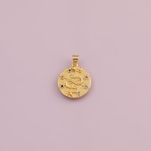 May include: Gold-coloured pendant with a snake design. The round pendant has a textured surface and is decorated with colourful gemstones. The snake is the central design element, and the pendant has a loop for a chain.
