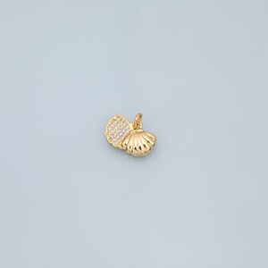 May include: A gold-colored seashell pendant with a small loop for a chain. One side of the shell is encrusted with small, clear crystals. The pendant is set against a light blue background.