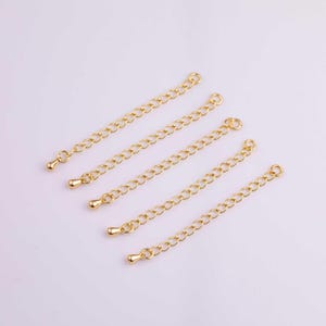 May include: Five gold-colored chain extenders. Each extender has a small loop on one end and a teardrop-shaped bead on the other. The chains are made of small, evenly spaced links.