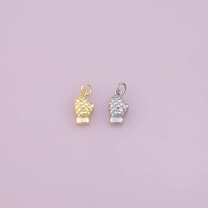 May include: Two small metal charms shaped like oven mitts, one in a polished gold tone and the other in a silver tone. Each charm features a detailed quilted texture across the surface and includes a small circular jump ring at the top.