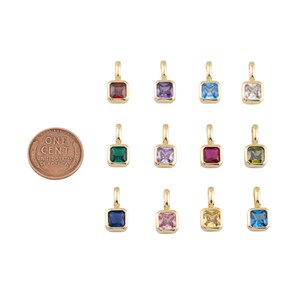 K&ouml;nnte beinhalten: Eine Sammlung goldfarbener quadratischer Anh&auml;nger mit verschiedenfarbigen Edelsteinen, darunter Rot, Lila, Blau und Gr&uuml;n. Eine Ein-Cent-M&uuml;nze dient zum Gr&ouml;&szlig;envergleich. Die Anh&auml;nger haben oben eine kleine Schlaufe zum Befestigen an einer Kette.